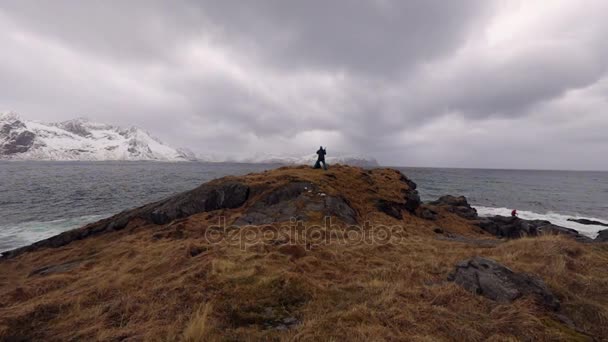 Фотограф-путешественник фотографирует древние камни на берегу холодного Норвежского моря в вечернее время. Лофотенские острова. Норвежский пейзаж. HD-кадры . — стоковое видео