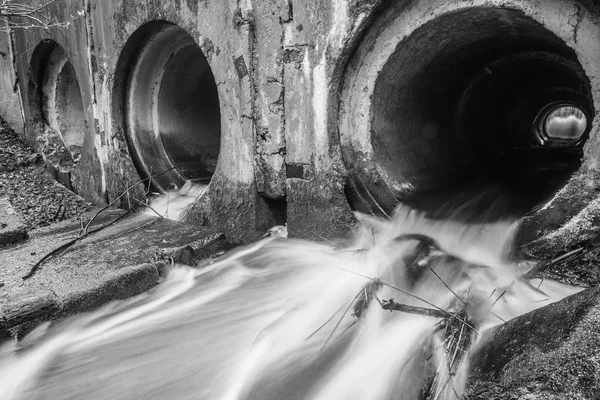 Barrage de rivière fait de tuyaux sous un pont dans une route forestière avec de l'eau courante. Photo noir-blanc . — Photo