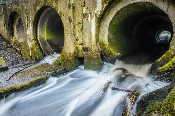 Barrage de rivière fait de tuyaux sous un pont dans une route forestière avec de l'eau courante . — Photo