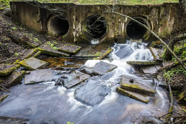 Речная плотина из труб под мостом в лесной дороге с проточной водой . — стоковое фото