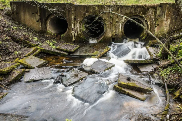 Rivier dam gemaakt van buizen onder een brug in een bos weg met stromend water. — Stockfoto