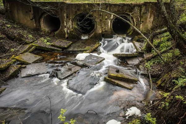 Flussdamm aus Rohren unter einer Brücke in einem Waldweg mit fließendem Wasser. — Stockfoto