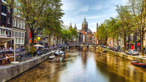 The most famous canals and embankments of Amsterdam city during sunset. General view of the cityscape and traditional Netherlands architecture.