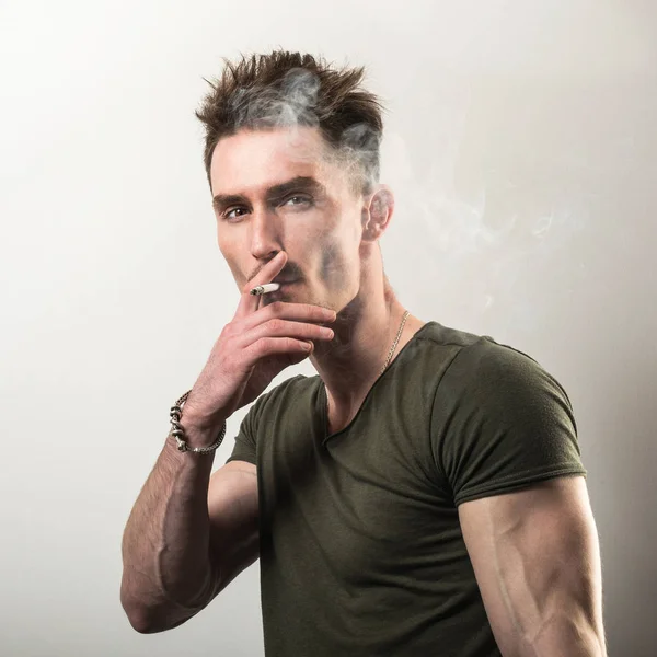 Schöner junger Mann in grünem T-Shirt mit Zigarette vor grauem Studiohintergrund. — Stockfoto