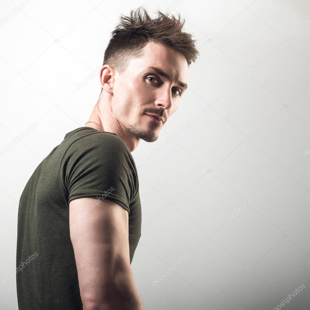 Handsome young sporty man in green t-shirt pose against gray studio background.