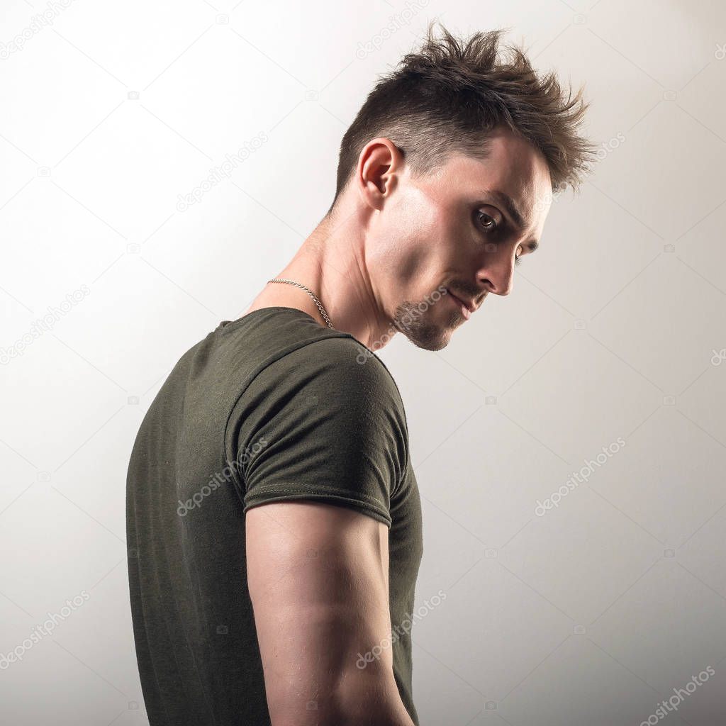 Handsome young sporty man in green t-shirt pose against gray studio background.