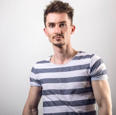 Çizgili gömlekli yakışıklı genç adam poz gri studio arka planı.