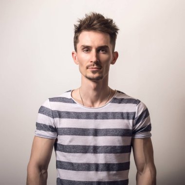 Çizgili gömlekli yakışıklı genç adam poz gri studio arka planı.