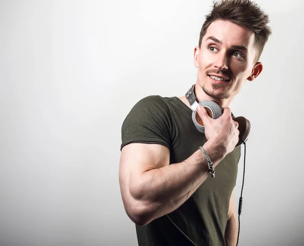 Handsome friendly sporty man in green t-shirt listening music against gray studio background. — Stock Photo, Image