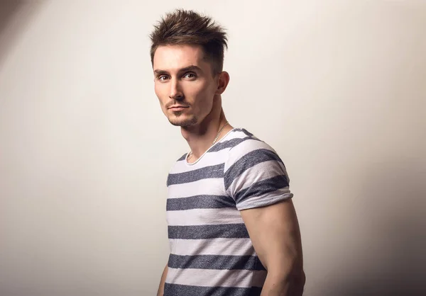 Красивый молодой человек в полосатой рубашке позирует на фоне серой студии . — стоковое фото