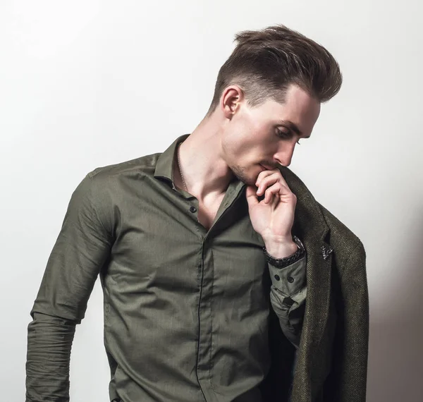 Beau jeune homme élégant en chemise verte pose sur fond de studio gris . — Photo