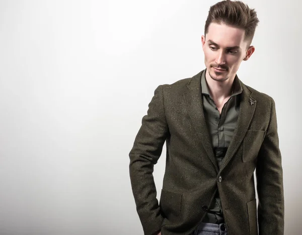 Beau jeune homme élégant en veste vert foncé pose sur fond de studio gris . — Photo