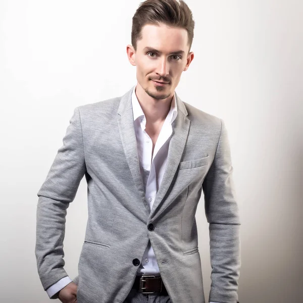 Guapo joven elegante hombre en gris chaqueta pose sobre fondo de estudio . —  Fotos de Stock