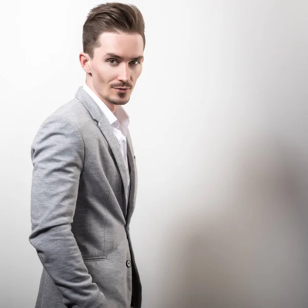 Schöner junger eleganter Mann in grauer Jacke posiert vor Studiohintergrund. — Stockfoto