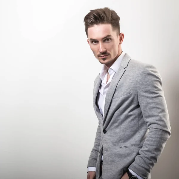 Guapo joven elegante hombre en gris chaqueta pose sobre fondo de estudio . —  Fotos de Stock