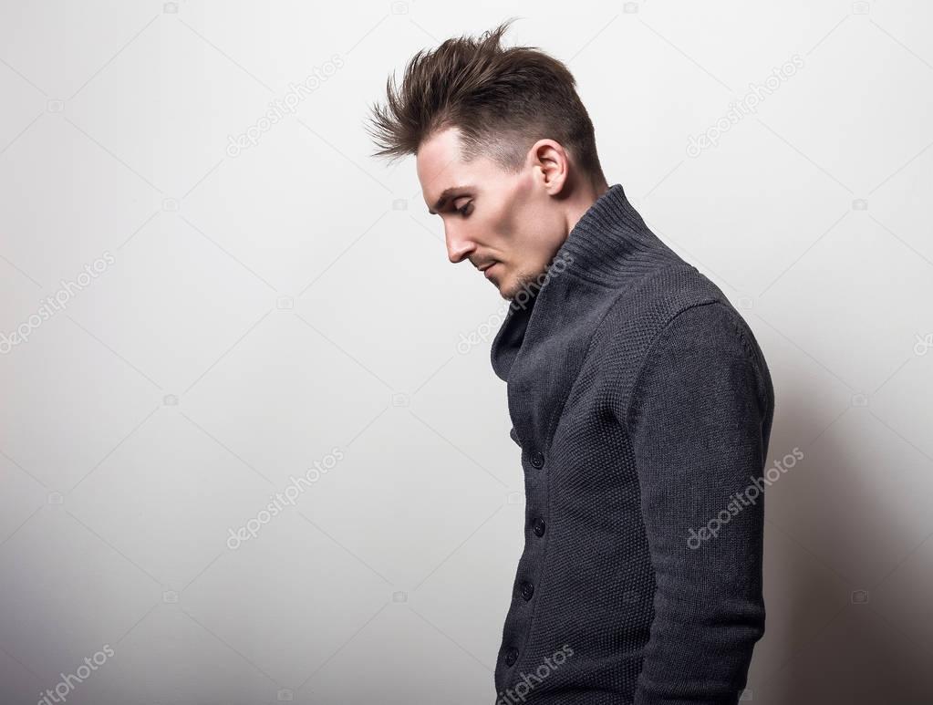Handsome young elegant man in grey switer pose against studio background.