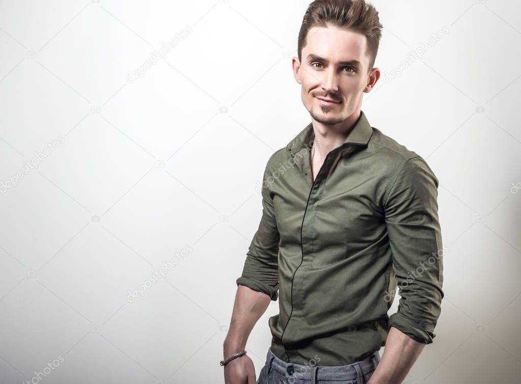 Handsome young elegant man in green shirt pose against gray studio background.