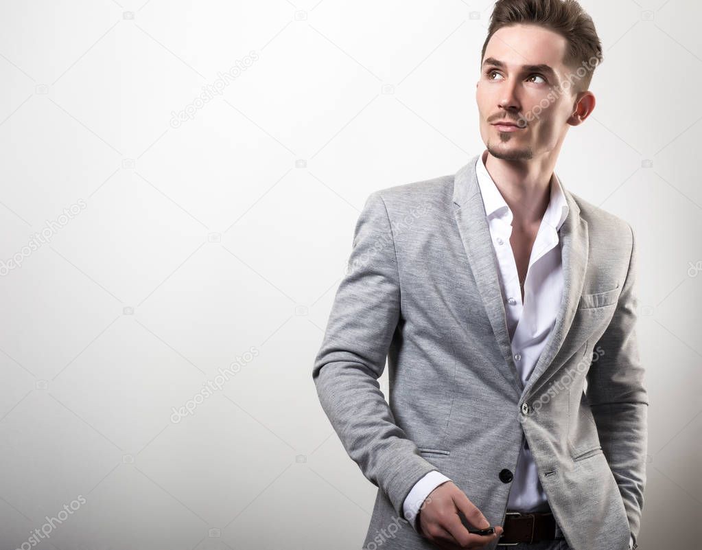 Handsome young elegant man in grey jacket pose against studio background.