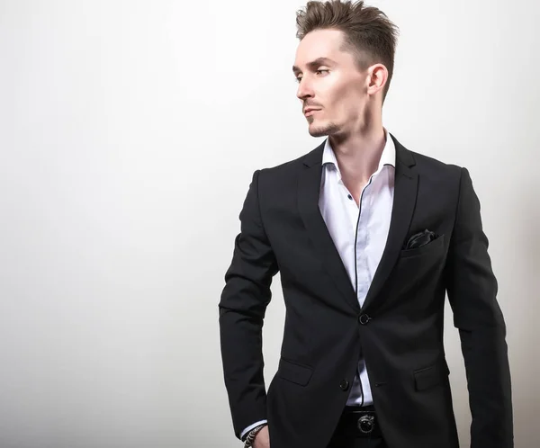 Guapo joven elegante hombre en negro elegante traje clásico pose contra fondo de estudio . — Foto de Stock