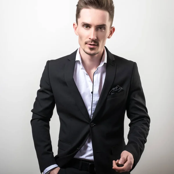 Beau jeune homme élégant en noir élégant costume classique pose sur fond de studio . — Photo