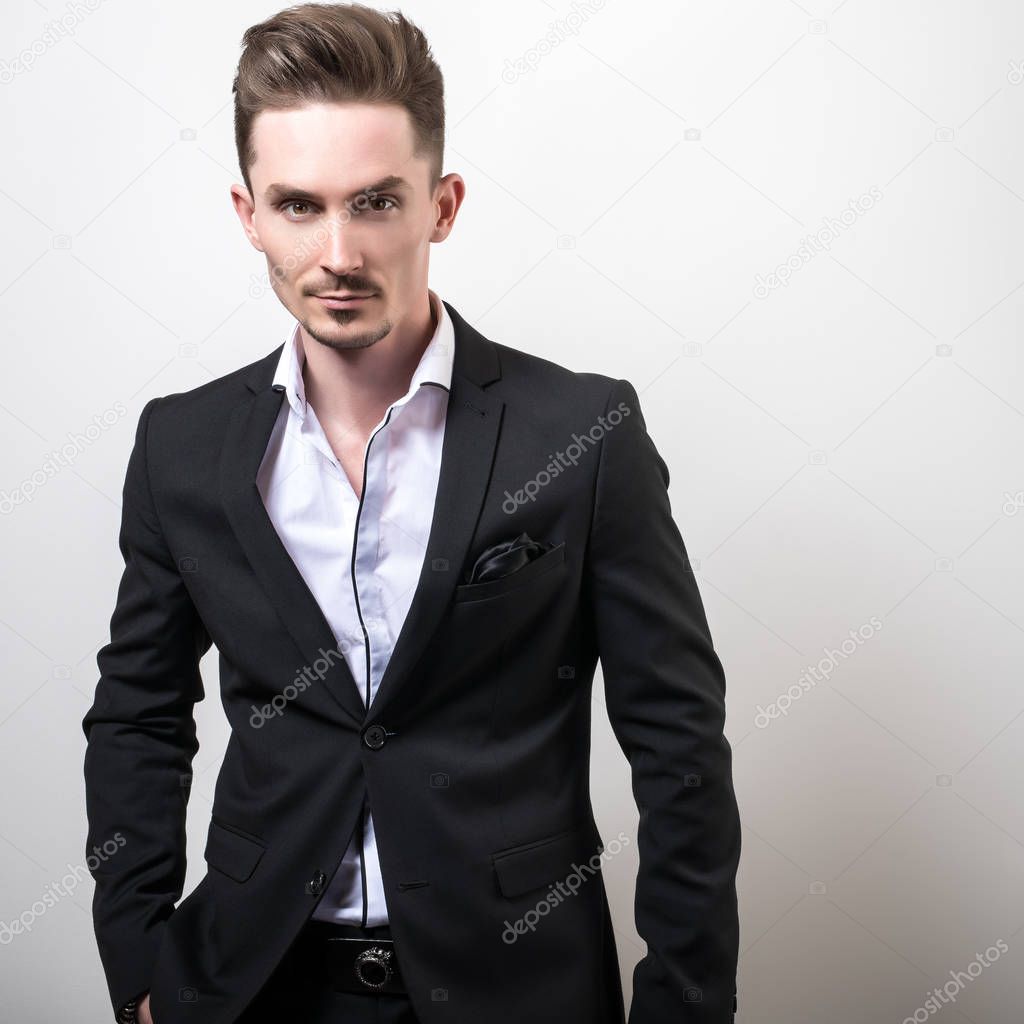 Handsome young elegant man in black stylish classic costume pose against studio background.