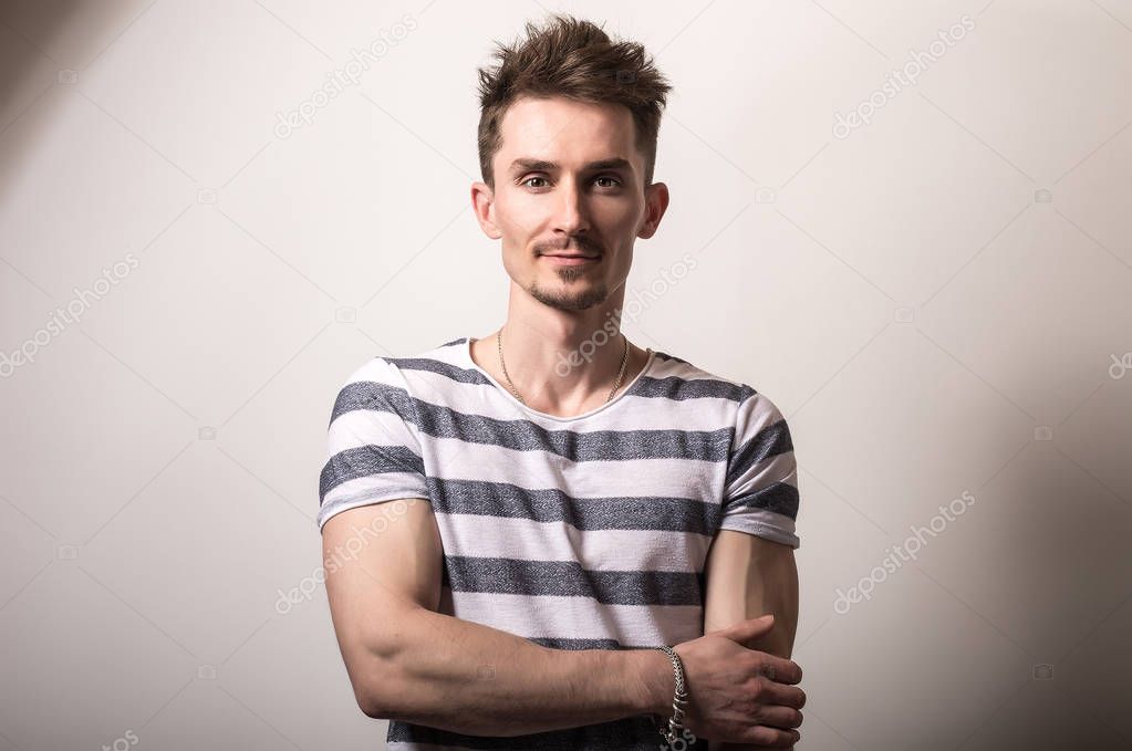 Handsome young man in striped shirt pose against gray studio background.