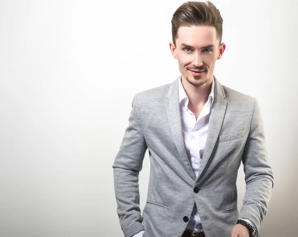 Guapo joven elegante hombre en gris chaqueta pose sobre fondo de estudio . — Foto de Stock