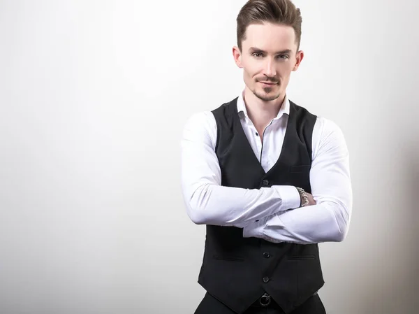 Bello giovane uomo elegante in nero classico gilet posa sullo sfondo dello studio . — Foto Stock