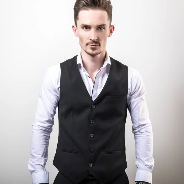 Bello giovane uomo elegante in nero classico gilet posa sullo sfondo dello studio . — Foto Stock