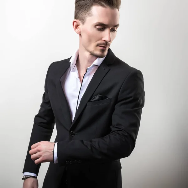 Beau jeune homme élégant en noir élégant costume classique pose sur fond de studio . — Photo