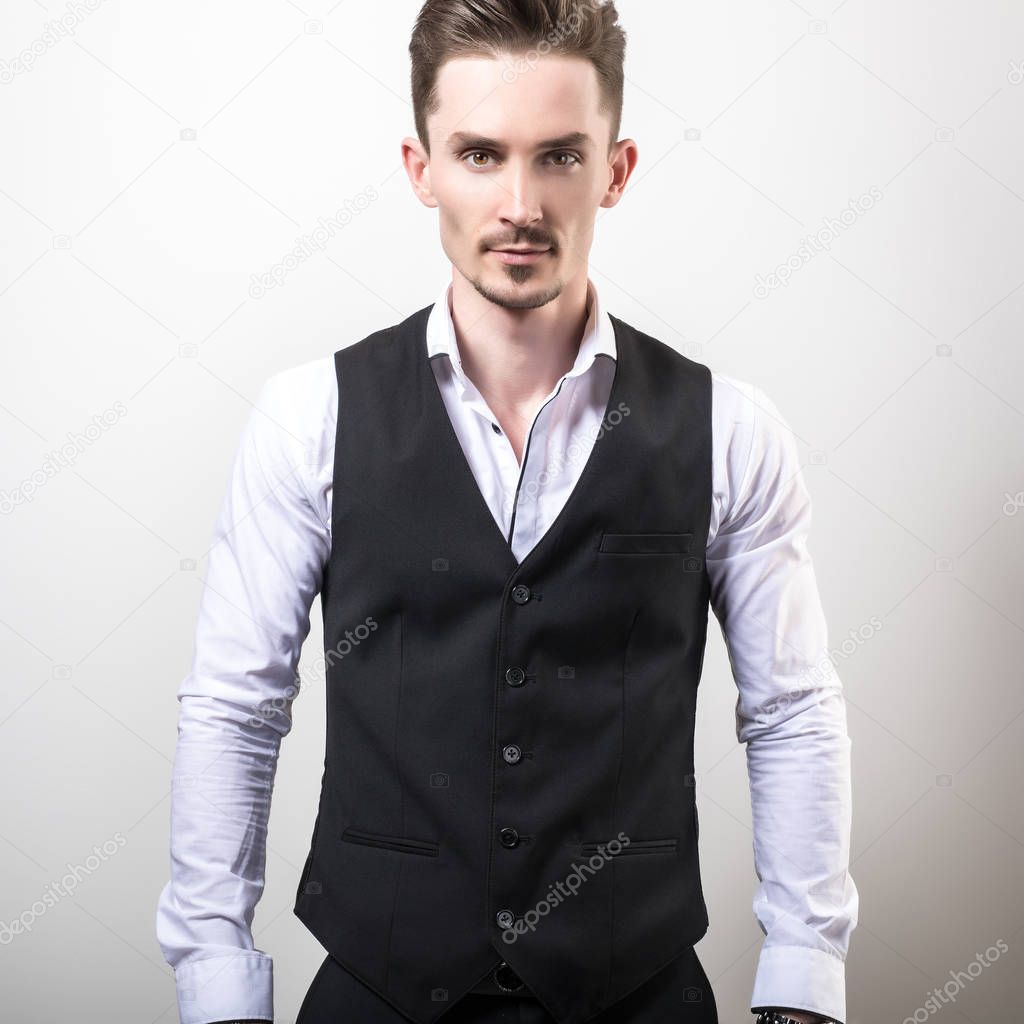 Handsome young elegant man in black classic vest pose against studio background.