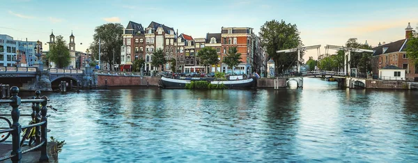 De meest beroemde grachten en ophogingen van Amsterdam tijdens zonsondergang. Algemeen beeld van het stadslandschap en de traditionele architectuur van Nederland. — Stockfoto