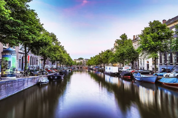 De meest beroemde grachten en ophogingen van Amsterdam tijdens zonsondergang. Algemeen beeld van het stadslandschap en de traditionele architectuur van Nederland. — Stockfoto