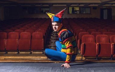 Actor dressed jester's costume in interior of old theater. 