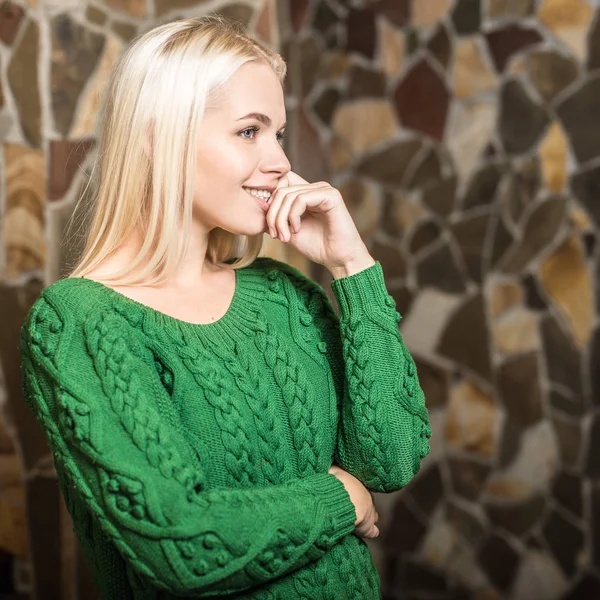 Молодая блондинка красотка в зеленом свитере против интерьера дома . — стоковое фото