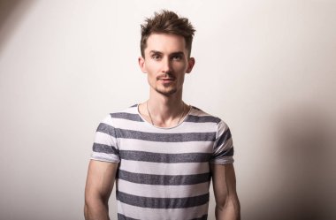 Çizgili gömlekli yakışıklı genç adam poz gri studio arka planı.