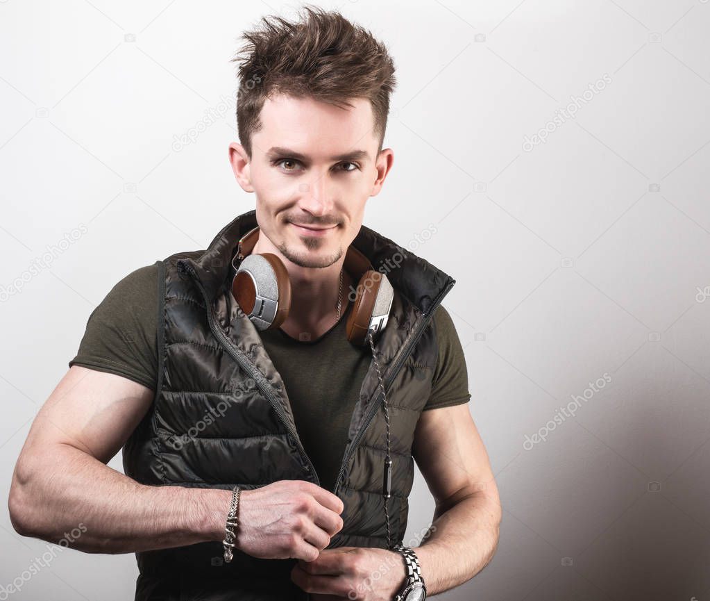 Handsome friendly sporty man in green t-shirt listening music against gray studio background.
