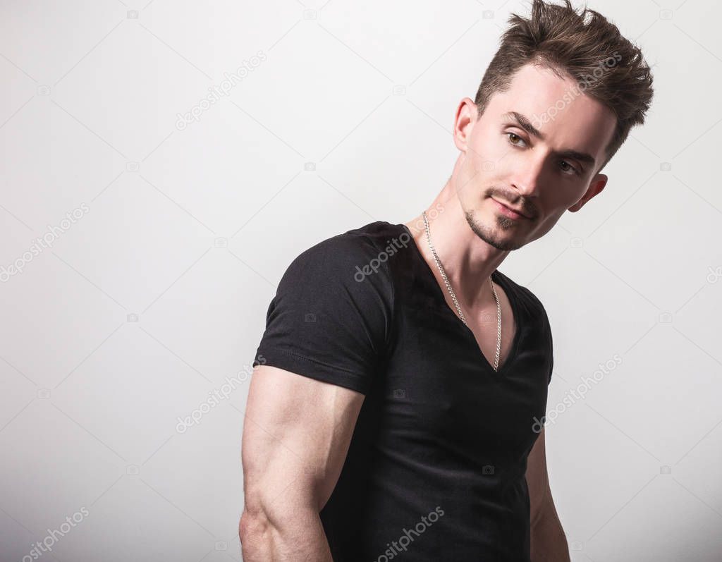 Handsome young sporty man in black t-shirt pose against gray studio background.