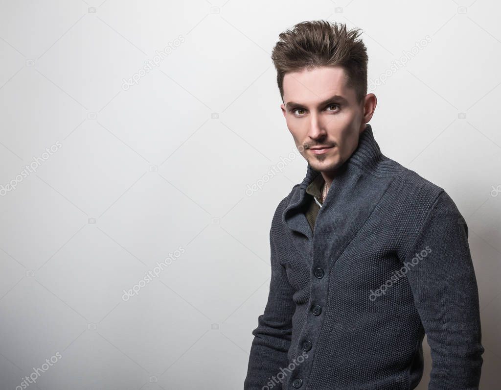 Handsome young elegant man in grey switer pose against studio background.