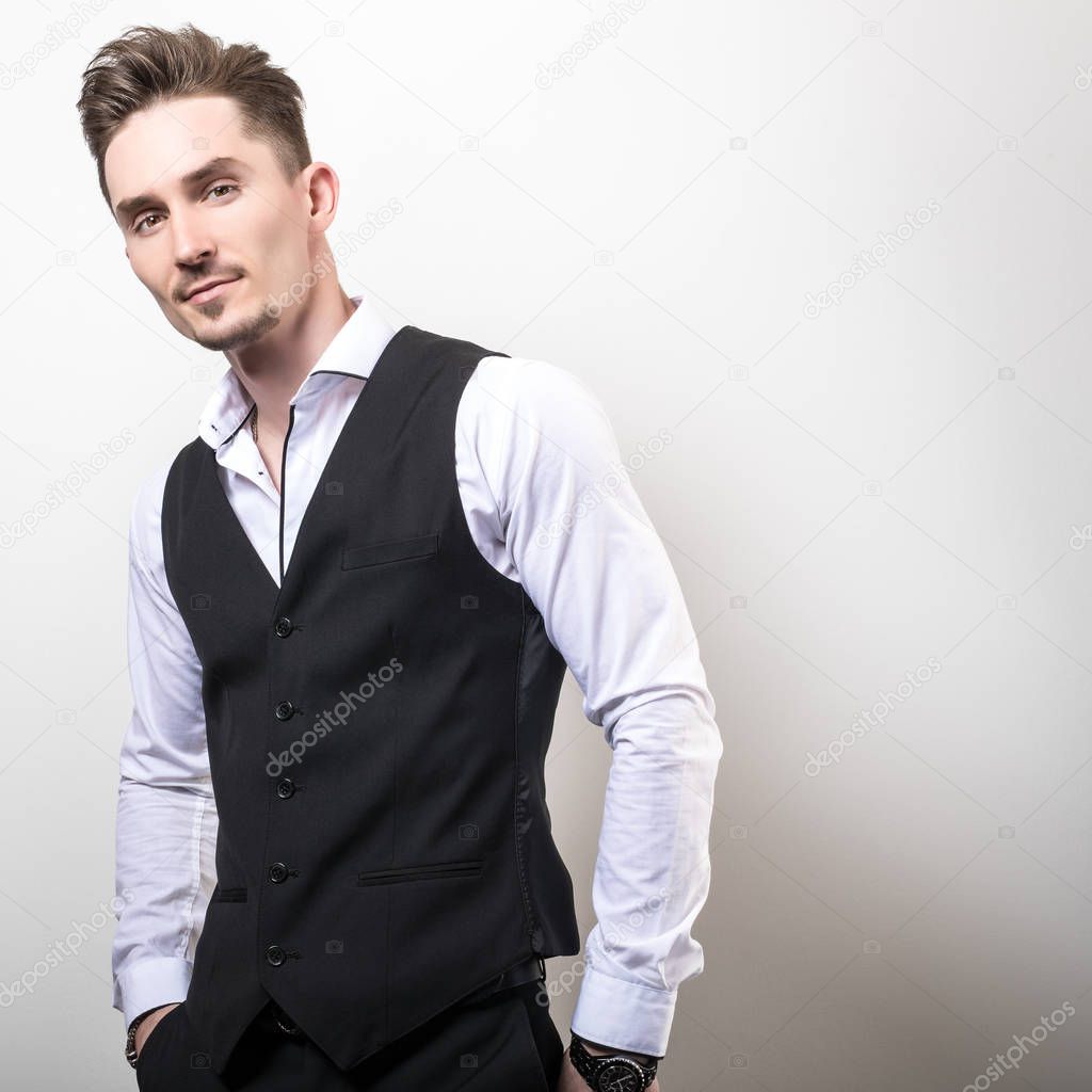Handsome young elegant man in black classic vest pose against studio background.