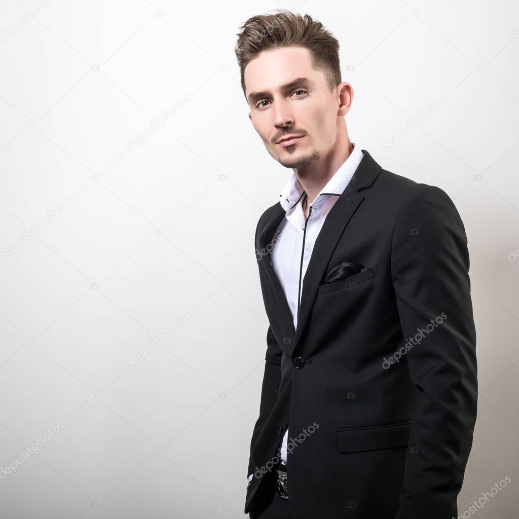 Handsome young elegant man in black stylish classic costume pose against studio background.