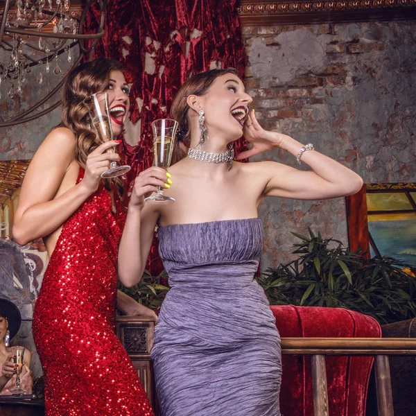 Twee jonge lachen stijlvolle meisjes gekleed klassieke stijl in het interieur van luxe club. — Stockfoto