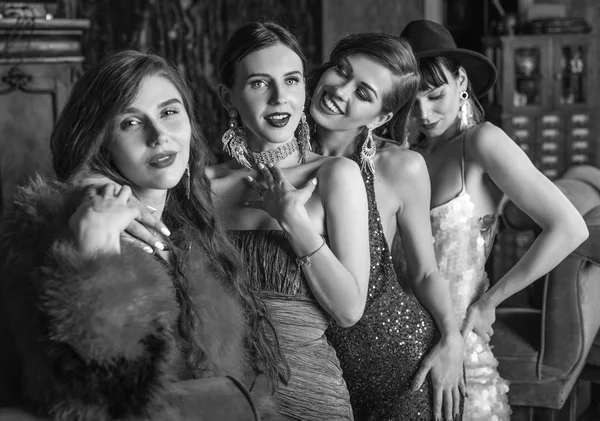 Grupo de jóvenes riendo elegantes chicas vestidas de estilo clásico en el interior del club de lujo. Foto en blanco y negro . —  Fotos de Stock