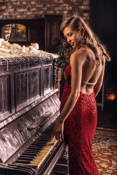 美丽的女孩在长的古典红色礼服摆着与老钢琴. — 图库照片