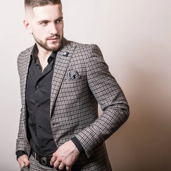 Bello giovane uomo elegante in giacca grigia posa contro lo sfondo dello studio . — Foto Stock