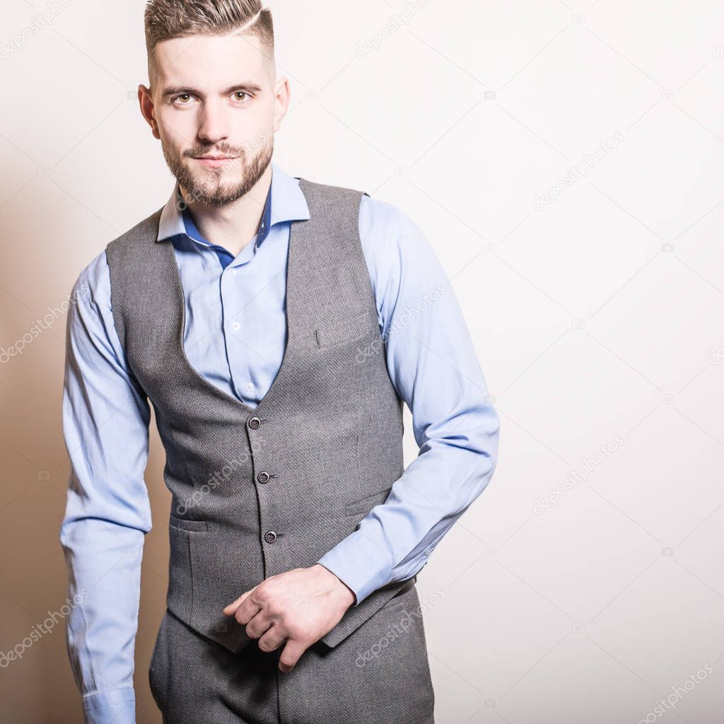 Handsome young elegant man in grey classic vest pose against studio background.