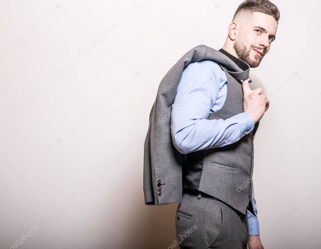 Handsome young elegant man in grey classic vest pose against studio background.