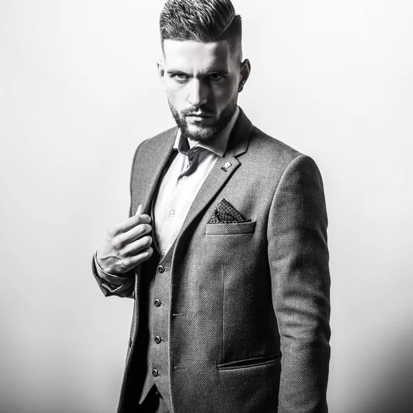 Schöner junger eleganter Mann in grauer Jacke posiert vor Studiohintergrund. Schwarz-Weiß-Porträt. — Stockfoto