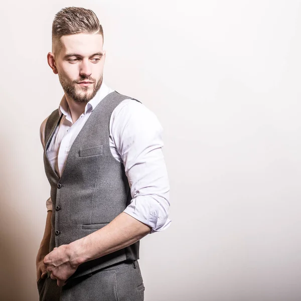 Schöner junger eleganter Mann in grauer klassischer Weste posiert vor Studiohintergrund. — Stockfoto