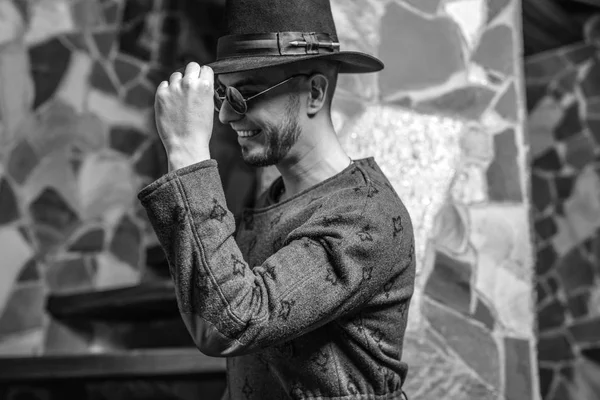 Guapo joven hombre con estilo en abrigo largo y sombrero sobre fondo de piedra . — Foto de Stock